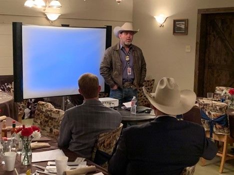 Man in a cowboy hat stands in front of a project screen facing a group of people